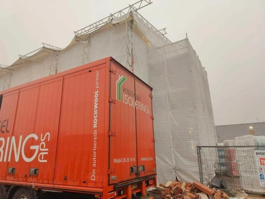 Byggeplads med isolerings lastbil og indpakkede stilladser.