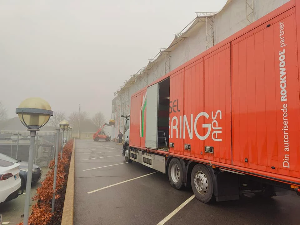 Orange lastbil parkeret ved lagerbygning i tåge